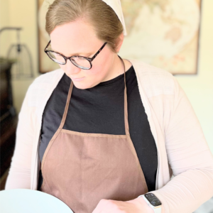 woman wearing apron holding mixing bowl and wooden spoon